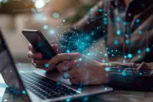 © Lucas / stock.adobe.com Person sitzt vor Laptop mit Smartphone in den Händen